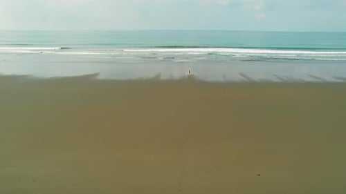 Einsamer Reisender, der am riesigen leeren dunklen Strand mit Blick auf die ruhigen Meereswellen spaziert