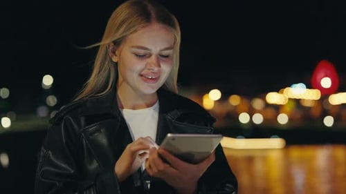 Smiling Lady Standing at Night City Scrolling Social Media on Tablet