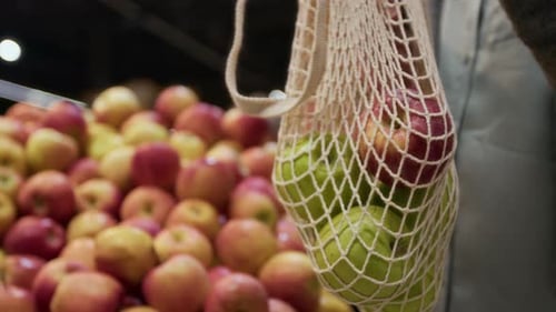 Primer plano de una mujer anónima poniendo manzanas en una bolsa de malla reutilizable en un supermercado