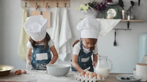 Zwei Kinder in weißer Kochuniform geben Mehl in die Schüssel in der Küche