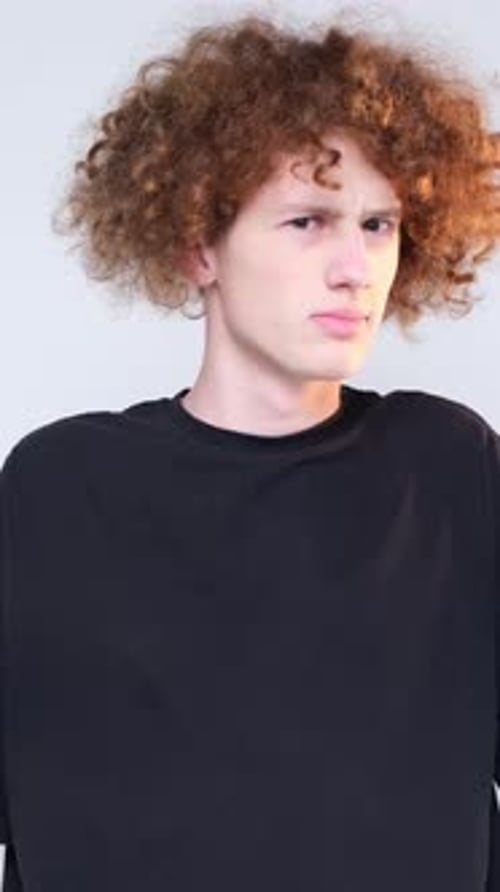 Porträt eines jungen lockigen Mannes in einem schwarzen T-Shirt auf hellblauem Hintergrund, der in die Kamera blickt