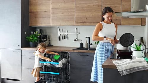 Woman Cooking as Child Empties Dishwasher in Kitchen