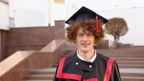 Happy Young Boy University Graduate in Traditional Black Bonet and Masters Mantle Standing with