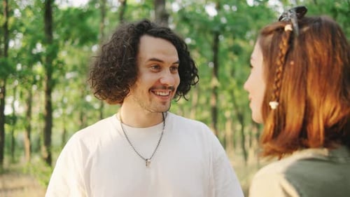 A Happy Couple of Tourists Talking After Hiking Against the Backdrop of Tents in a Lush Forest