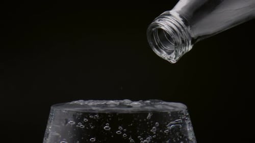 Water Bottle Pouring Liquid into Glass on Black