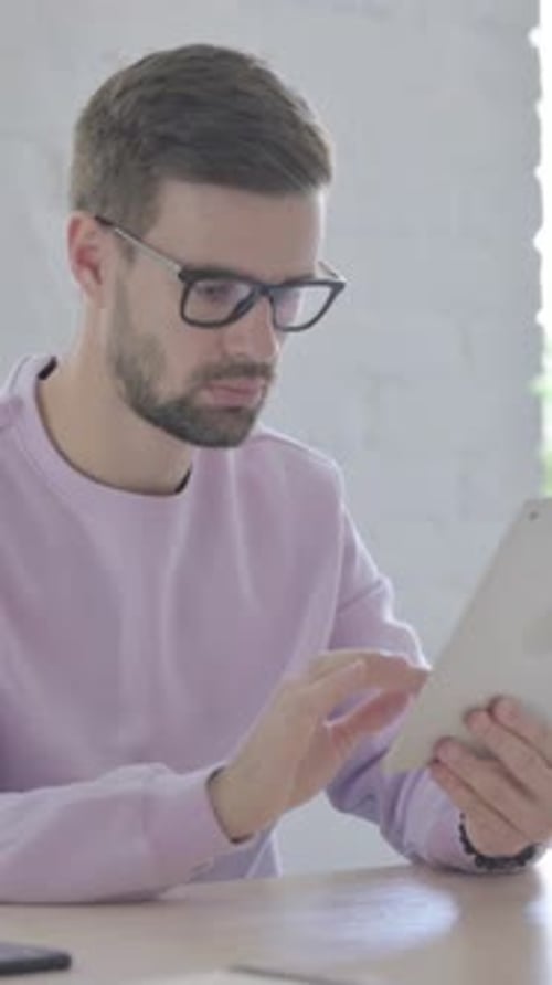 Man Uses Tablet While Sitting at Desk Indoors