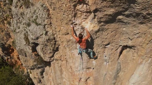 aerial slow motion filming from drone strong muscular man rock climber climbs on vertical cliff