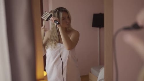 Woman Styles Blonde Hair with Waver in Mirror