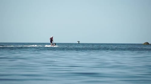 A Motorized Surfboard with a Rider Moving on a Calm Sea The Silhouette of a Man on a Water Scooter