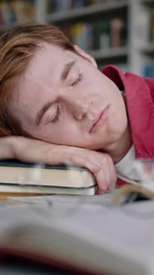 Redhead Man Falls Asleep Lying on Stack of Books on Desk