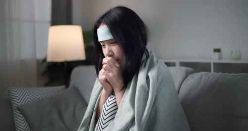 Jeune femme asiatique malade maux de tête fièvre toux rhume éternuements assise sur le canapé dans le salon à la maison.