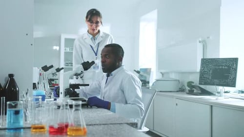 Close Up Two Scientists in Uniform Looking Under a Microscope Talking Discuss in the Laboratory