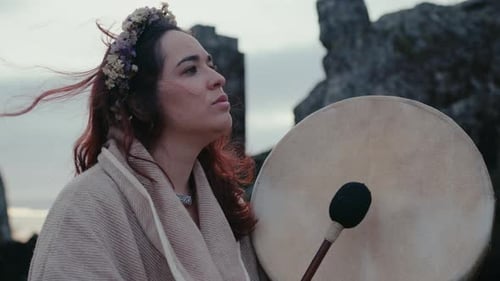 spiritual woman playing a shamanic drum in a beautiful with a old medieval tower behind her close sh