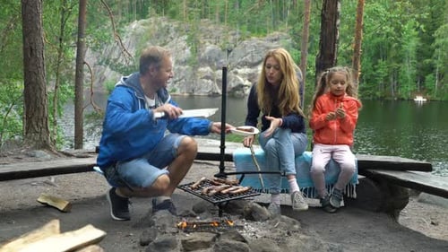 A Couple with a Child Grilling in the Forest on the Shore of the Lake