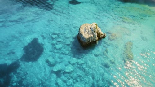 Vue aérienne d'un rocher isolé dans une eau turquoise peu profonde avec des détails visibles sur le fond marin