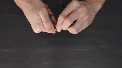Man Cuts Wire with Knife on Wooden Table in Closeup