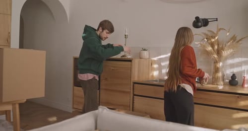 Focused Blond Guy and His Girlfriend Take Things Out of Cardboard Boxes and Place Them on Furniture