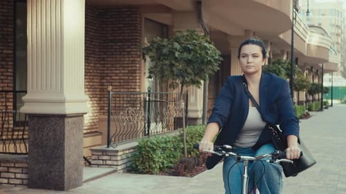 A Businesswoman Goes to Work in the Office on a Bicycle in an Urban Landscape