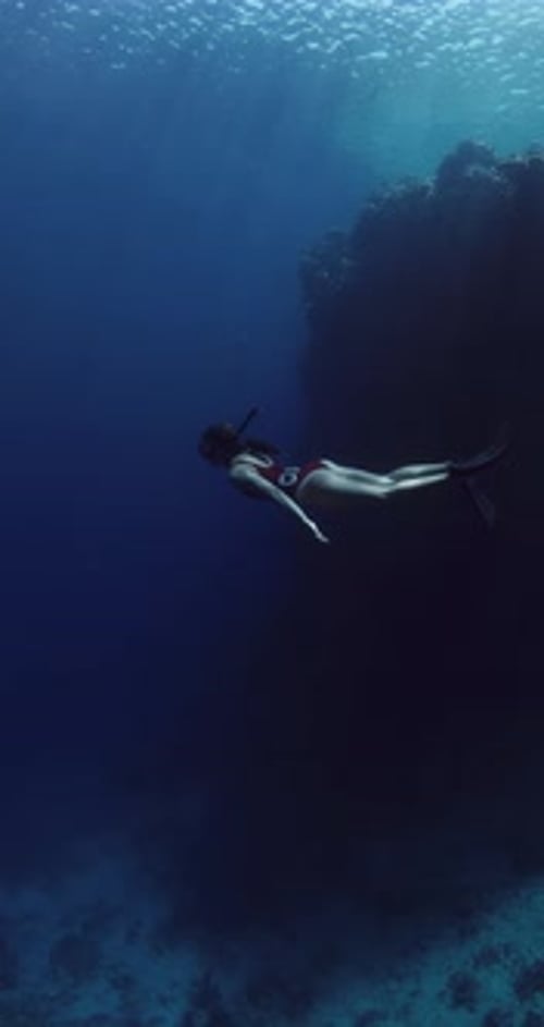 Freediver Swims in Deep Ocean with Sun Rays Woman Freediving in Deep Sea Near Rocks