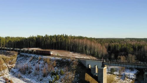 Cargo train crossing bridge during winter. Aerial view.