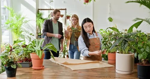 A Young Asian Female Gardener in a Home Gardening Store Helps a Couple Select an
