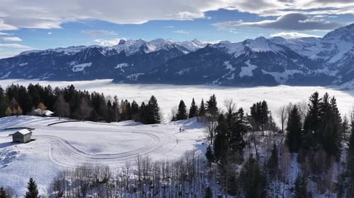 aerial - snowy hillside and forest overlooking a bright cloud ocean in churfirsten