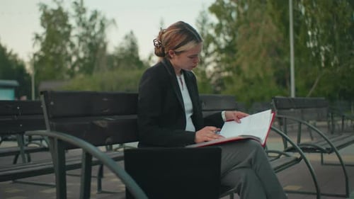 Side View Girl Focused Reading Outdoor with Book Coffee Laptop and Urban Background