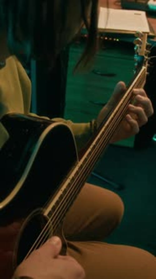 Vertikale Darstellung eines Gitarristen, der ein Lied auf einer Akustikgitarre im Studio mit Neonlicht spielt
