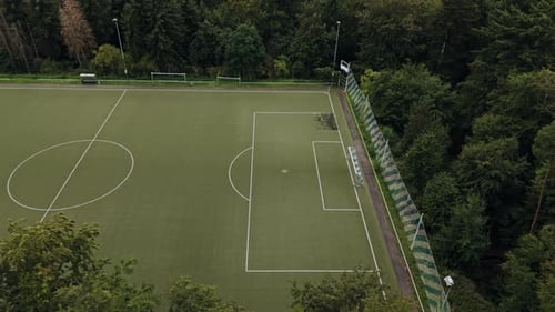 Aerial Flight besides an empty, green football field in the middle of the forest, Drone Footage