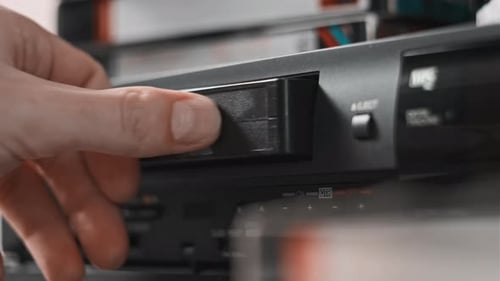 Male Hand Inserts VHS Cassette Into a VCR Video Recorder