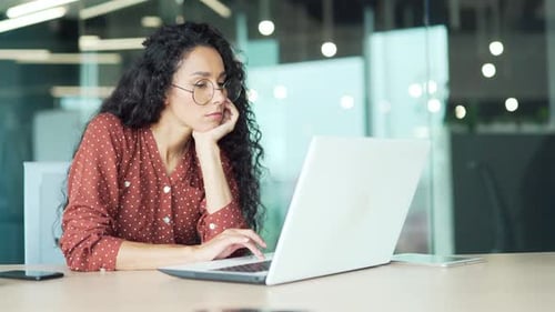 Thoughtful young businesswoman bored working on laptop sitting at workplace in business office.