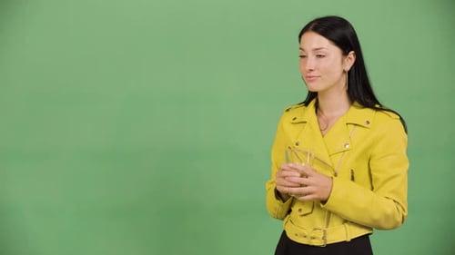 Eine junge kaukasische Frau trinkt Wasser aus einem Glas und lächelt dann in die Kamera (Green Screen)
