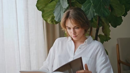 Pretty Lady Looking Magazine Sitting Cozy Apartment with Green Plant Closeup