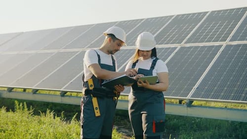 Wartungspersonal auf einem Feld mit Sonnenkollektoren, die Daten auf einem Tablet sammeln