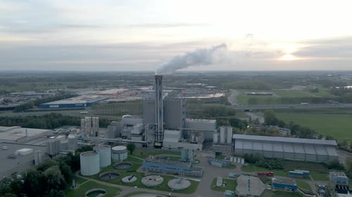 Aerial dolly of smoking factory chimney with a setting sun in the background