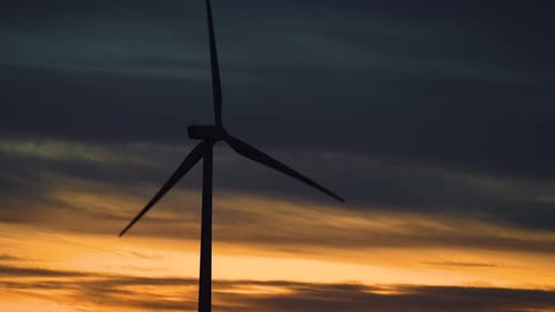 Rotierende Rotorblätter großer Windturbinen im Feld vor dem Hintergrund eines Dramatisch, bewölkten, rosa-orangen Sonnenuntergangs