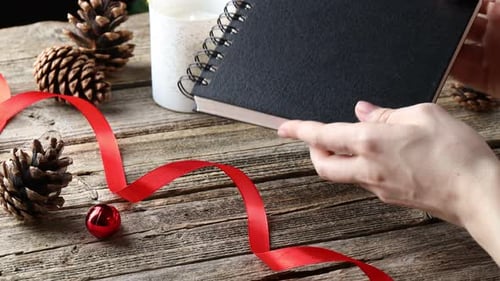 New Year aims. Woman holding planner at wooden table with festive decor, closeup