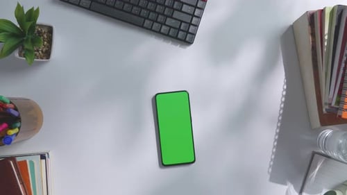 Top down view of a mock up green screen smartphone on a white office desk