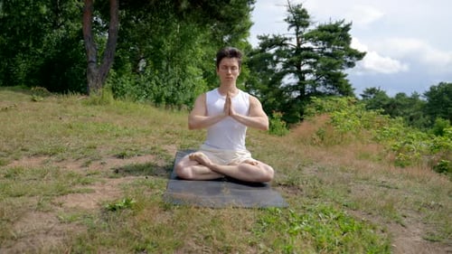 Young Athletic Man Meditates in Lotus Pose on Grassy Meadow
