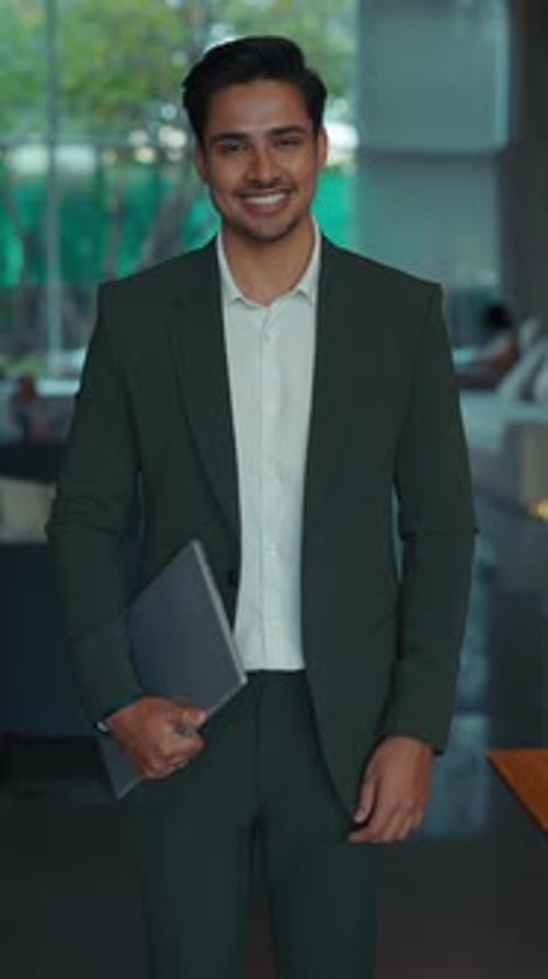 Smiling Man in Suit Holding Laptop Indoors