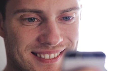Smiling man looking at his smartphone close-up