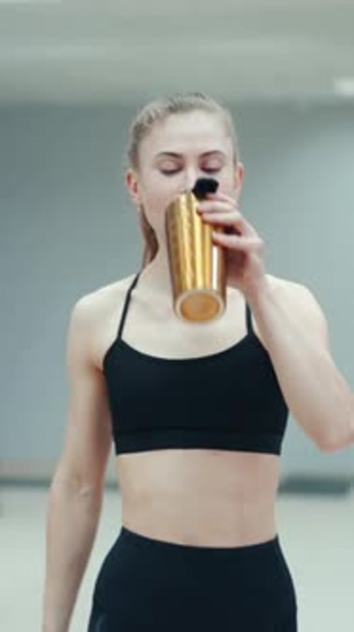 Pretty woman in a black top is drinking a drink from a yellow shaker
