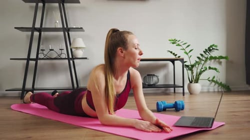 Junge schöne Frau wiederholt Dehnübungen aus dem Video-Tutorial zu Hause und schaut sich das Training an