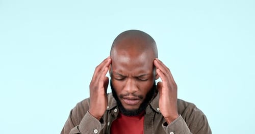 Man, headache and pain in studio for stress, vertigo and burnout on blue background