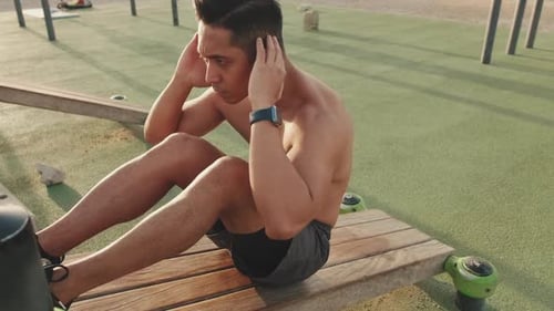 Junger Mann trainiert draußen Bauchmuskeln auf dem Sportplatz