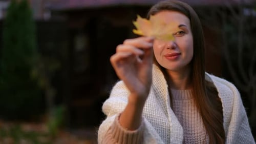 Eine wunderschöne herbstliche Reflexion Eine junge Frau, die ein Ahornblatt in einer gemütlichen Umgebung hält