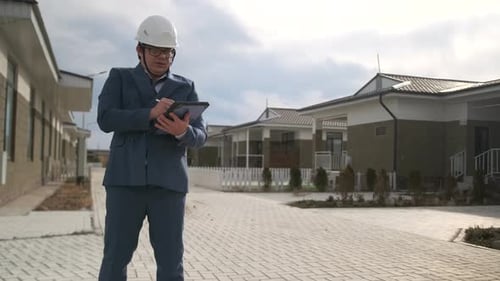 Inspector in helmet with clipboard making notes examining a built street in a cottage community