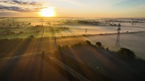 Electrical Towers Rising Over Foggy Landscape at Sunrise