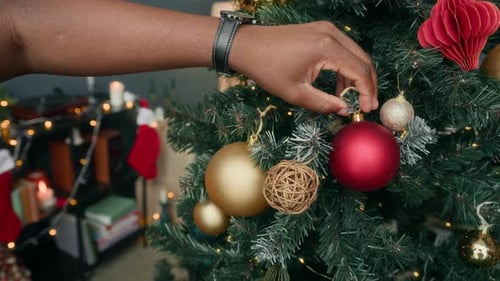 Man Decorates Christmas Tree at Home with Ornaments