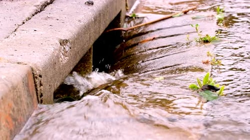 Rainwater after downpour runs down concrete gutter into street drain, hydrology